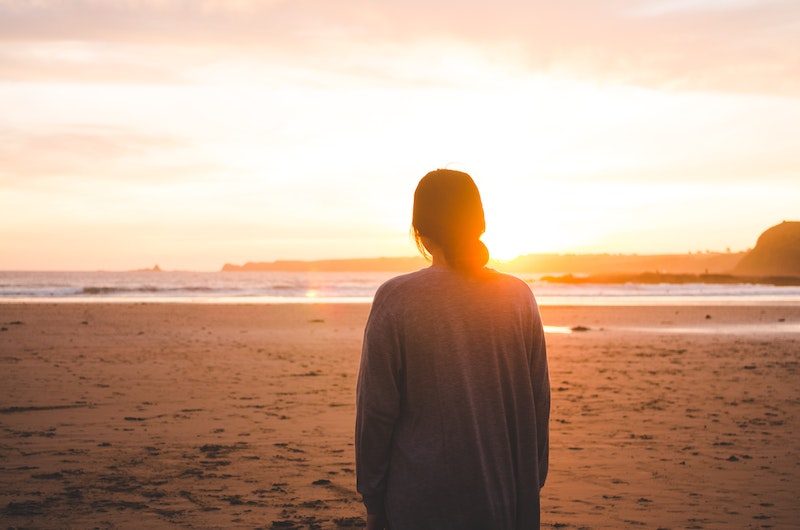 Back on woman standing on shore during sunset