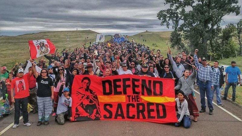 Hundreds of people with red sign that says "Defend the Sacred"