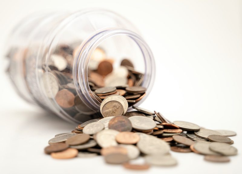 US coins falling out of clear jar on white background