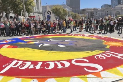 A red circle that says "Sacred" painted on the ground with a group of people in the background in San Francisco