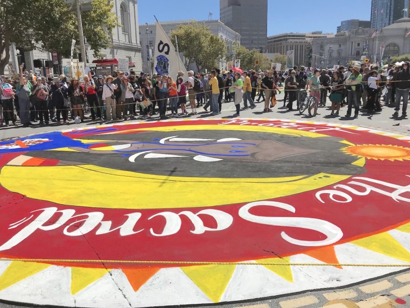 A red circle that says "Sacred" painted on the ground with a group of people in the background in San Francisco