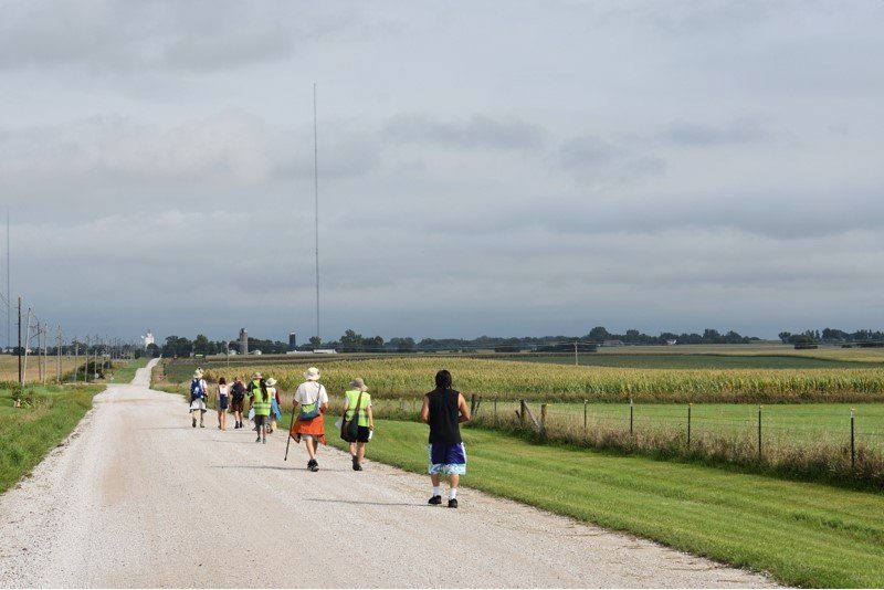 A few people walking ona very straight, flat highway