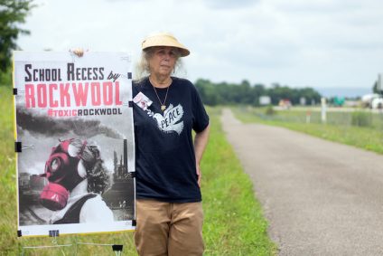 Bobbi Block holding up Rockwool protest poster next to country road
