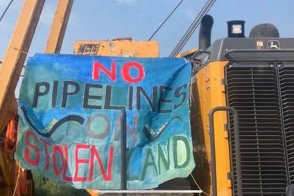 Painted blue banner with text "No Pipelines on Stolen Land" hanging on large machinery