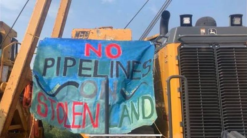 Painted blue banner with text "No Pipelines on Stolen Land" hanging on large machinery