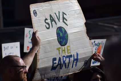Man with glasses holding up cardboard sign that says "Save the Earth"