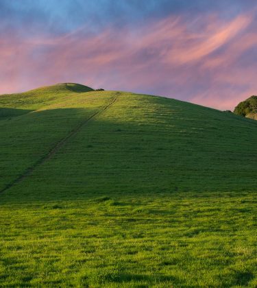 Green grassy hill with path to the top and blue sky with pink clouds