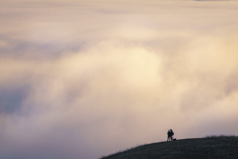 Silhouette of a person at the top of a hill, with huge clouds beyond the person and hill taking up most of the picture